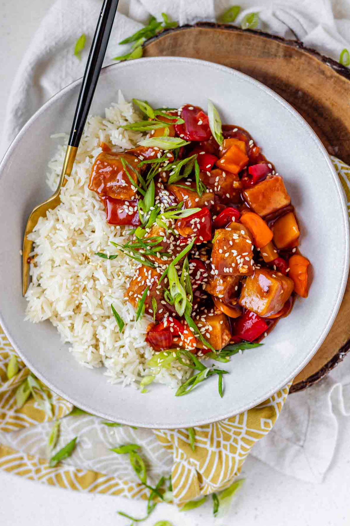 Tofu in sauce in a bowl beside rice, garnished with green onions.