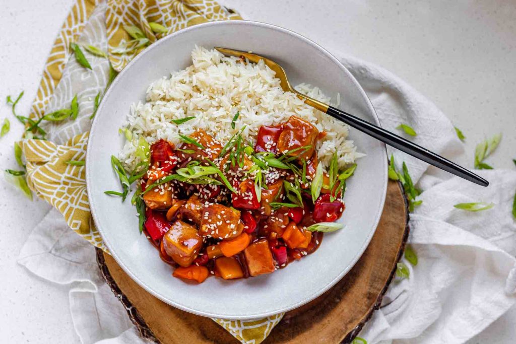 Tofu in sauce in a bowl beside rice, garnished with green onions.