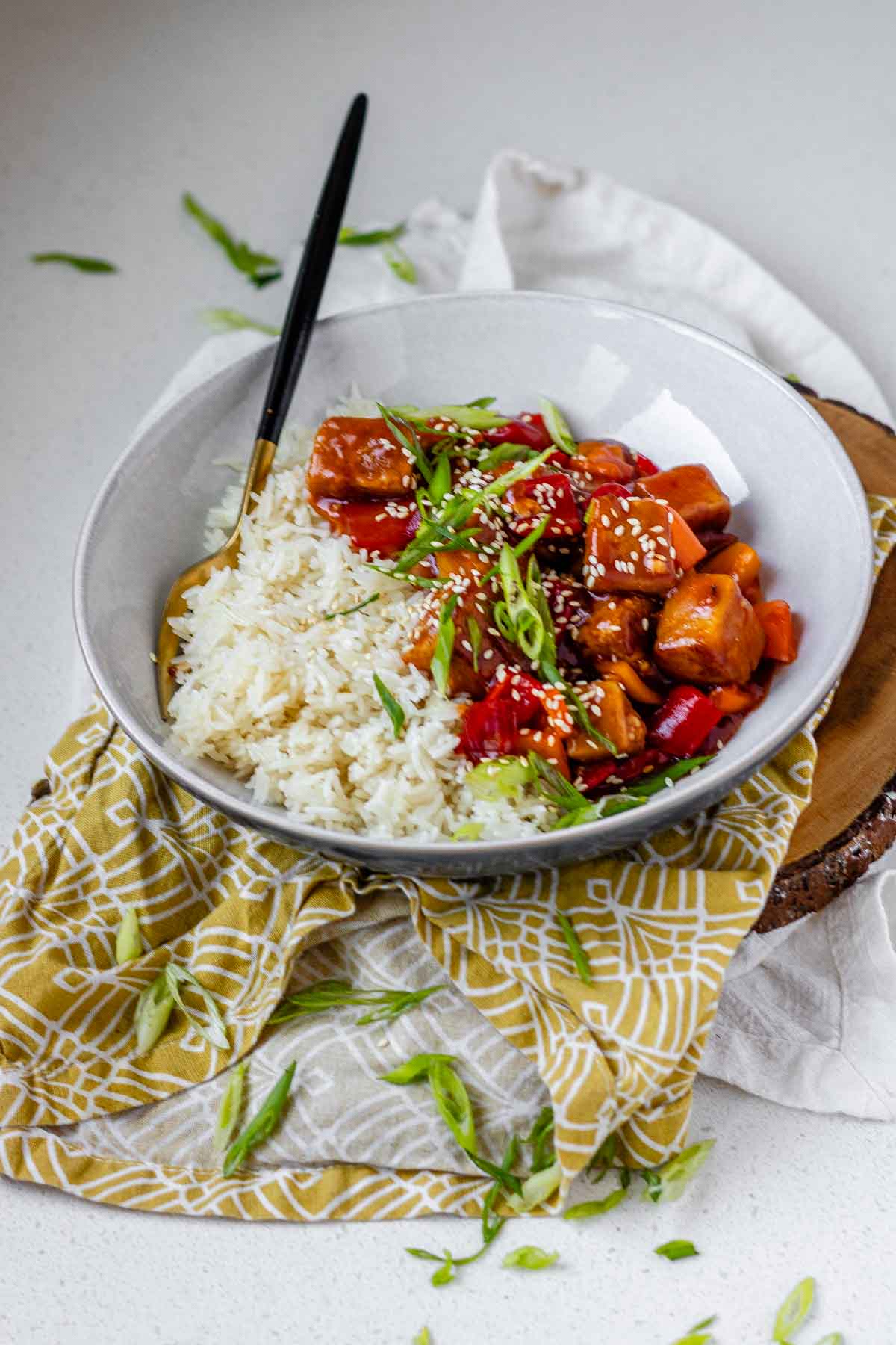 Tofu in sauce in a bowl beside rice, garnished with green onions.