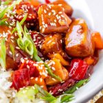 Tofu in sauce in a bowl beside rice, garnished with green onions with the text sweet and sour tofu.