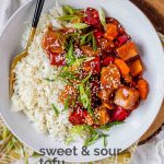 Tofu in sauce in a bowl beside rice, garnished with green onions with the text sweet and sour tofu.