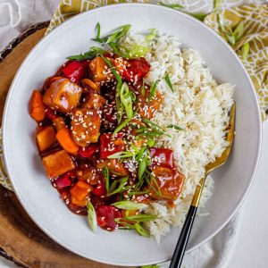Tofu in sauce in a bowl beside rice, garnished with green onions.
